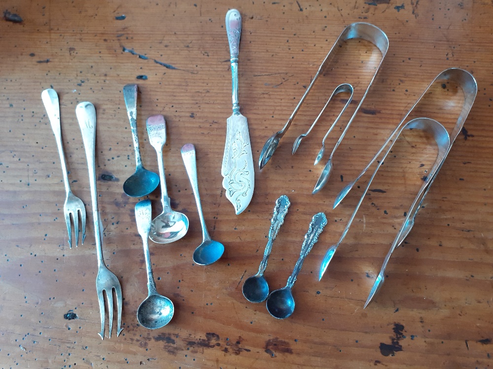 A collection of silver flatware comprising sugar tongs, butter knife, pickle forks,mustard spoons et