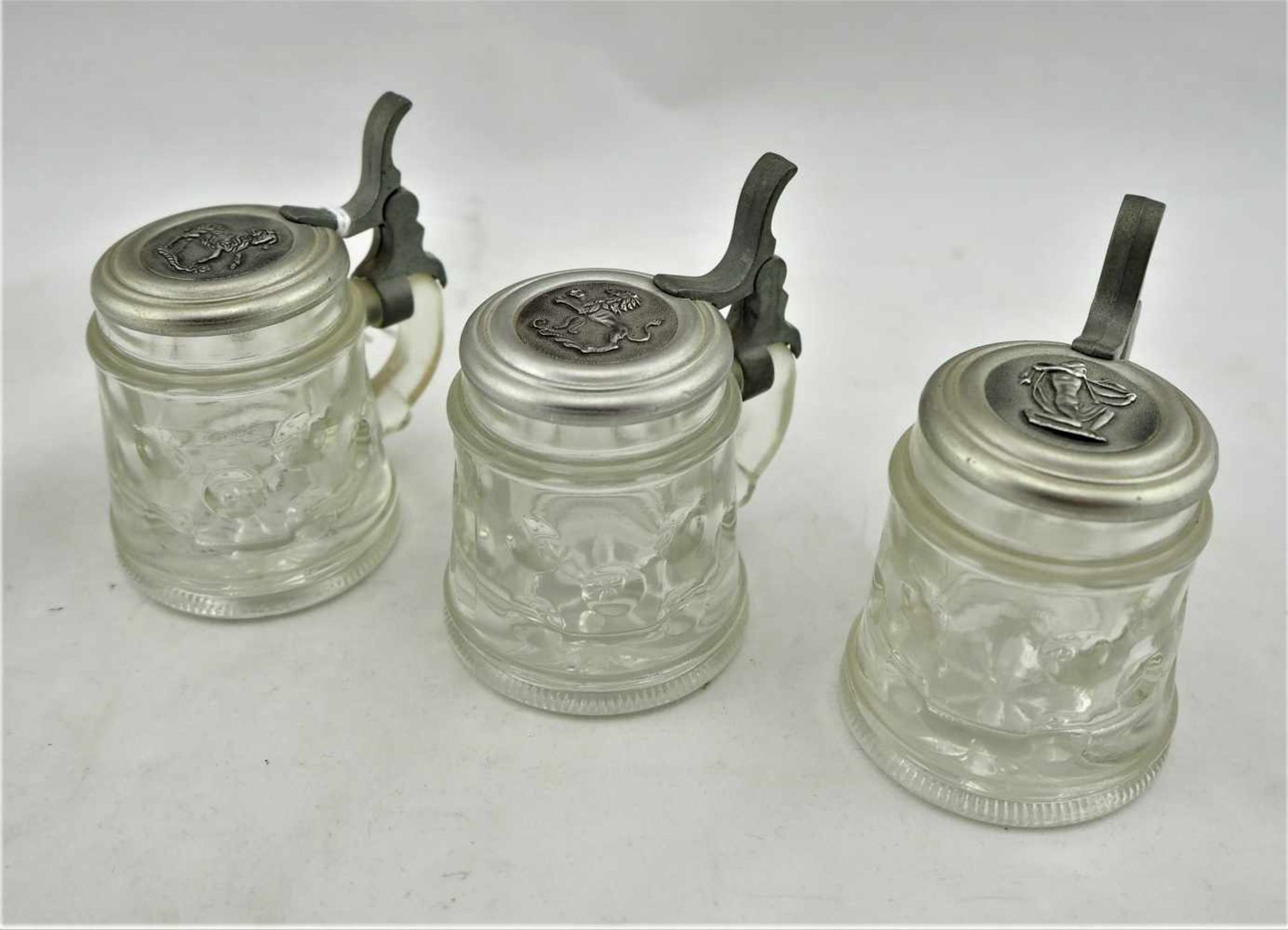 Drei MinikrügeAus Klarglas mit Handhabe und Zinndeckel. Gesamt drei Stück, alle intakt. H.7cm, Ø4,