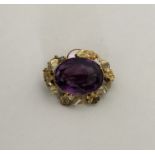 An amethyst single stone brooch in gold floral fra
