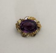 An amethyst single stone brooch in gold floral fra