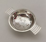 An Art Deco silver tea strainer with engraved deco