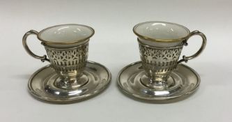 A pair of silver and porcelain cups and saucers. A