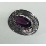 An oval silver brooch decorated with an amethyst.