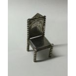A miniature silver chair with engraved decoration.