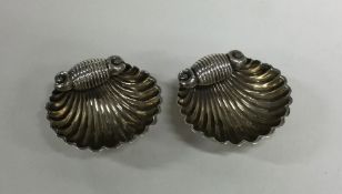 A pair of silver shell shaped salts on ball feet.