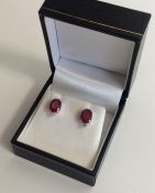 A pair of ruby and diamond oval ear studs in claw