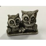 A modern silver model of two owls perched upon a b
