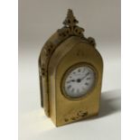 A small brass travelling clock of Gothic design wi