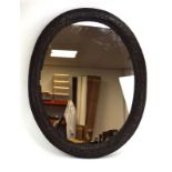 An 18th century wall mirror with a carved oak scrollwork and acanthus leaf oval frame,