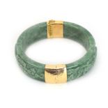 A mottled green jade hinged bracelet, carved with foliate motifs and mounted in 14ct yellow gold,