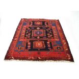 An Iranian rug, the red ground with a central medallion and stylised black and blue motifs,