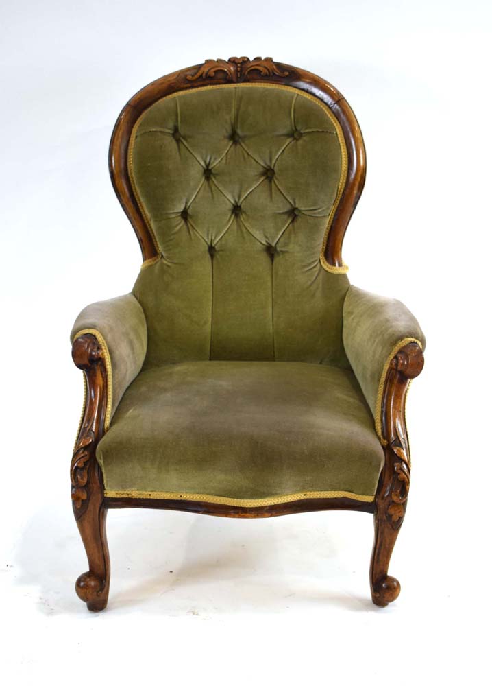 A Victorian walnut and button upholstered fireside armchair on scrolled feet with castors