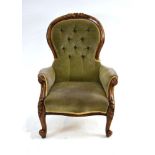 A Victorian walnut and button upholstered fireside armchair on scrolled feet with castors