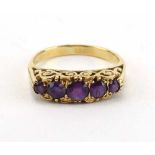 A yellow metal ring set five graduated amethyst in a scrolled setting, ring size T 1/2,