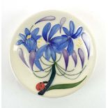 A Moorcroft pin dish of circular form, decorated with blue flowers and a ladybird on a white ground,