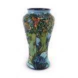 A Moorcroft vase of slender baluster form decorated with a woodland scene on a shaded blue ground,