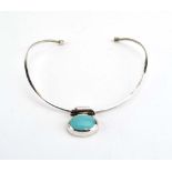 A modern silver torque style necklace suspending an oval turquoise pendant