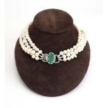A triple strand continuous cultured pearl necklace with an 18ct white gold clasp set emeralds and