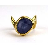 A modern yellow metal ring set cabochon star sapphire in a rubover setting with wavy edge band,