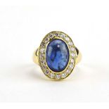 A yellow metal cluster ring set oval cabochon sapphire within a border of brilliant cut diamonds,