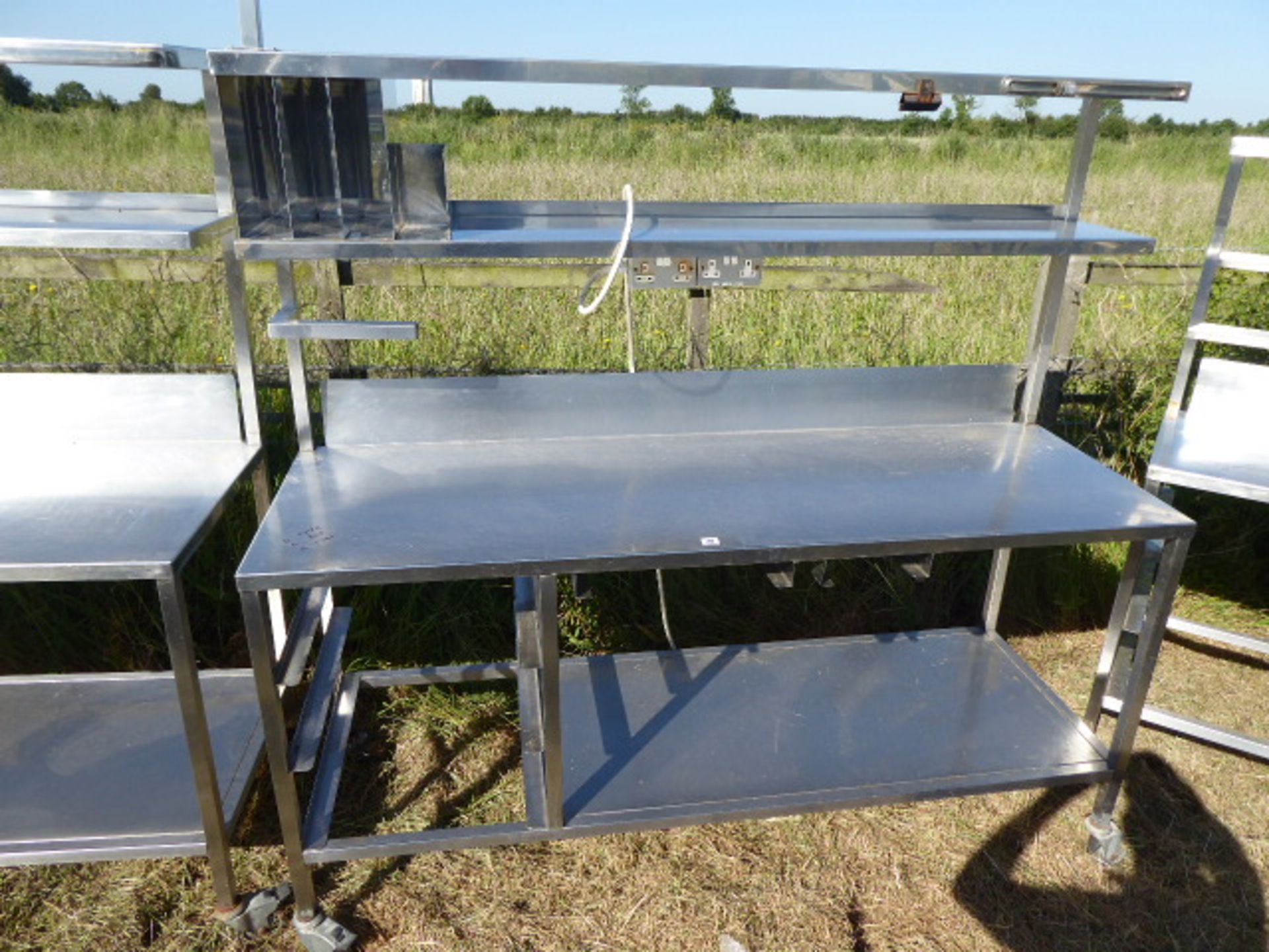 Stainless steel mobile food preparation station with 2 shelves over, shelf under space for trays,