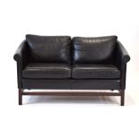 A 1970's Stouby black leather two-seater sofa with scrolled arms on stained beech legs joined by