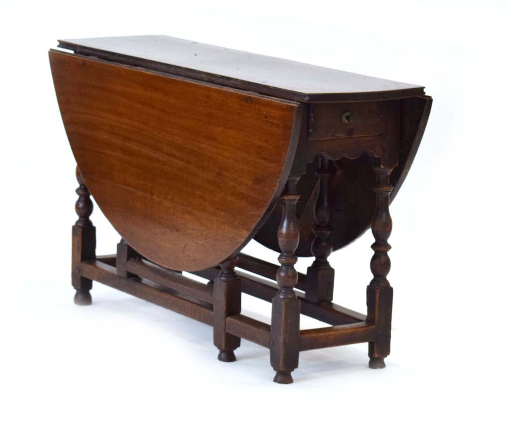 An 18th century oak gateleg table with a single frieze drawer on turned supports joined by