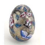 A metalware and champleve enamelled egg decorated with flowering shrubs and insects,