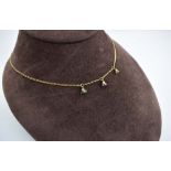 A 9ct yellow gold figaro link necklace suspending three small drops each set a small diamond,