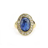 A yellow metal cluster ring set oval cabochon sapphire within a border of brilliant cut diamonds,