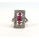 A white metal ring set three graduated square cut rubies within a rectangular diamond set