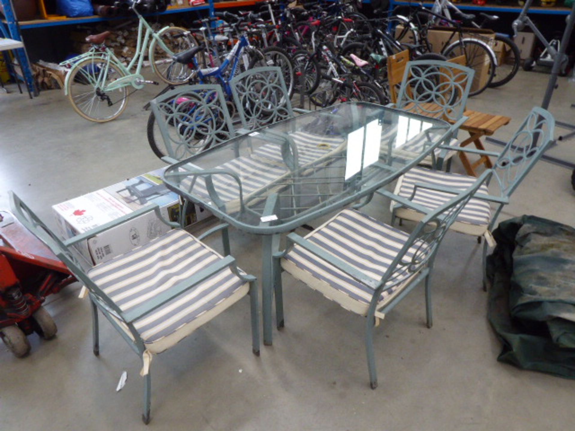 Oval glass topped table on green metal supports with 6 matching chairs and cushions