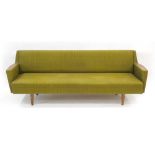 A 1970's green fabric three-seater daybed with teak detail to the arms and tapering legs, l.