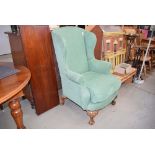 Green fabric wingback armchair with carved frame