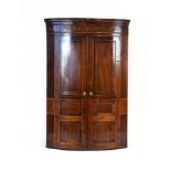 A George III mahogany, strung, crossbanded and inlaid bow-fronted corner cabinet, wall-mounted,