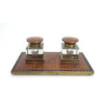 An Edwardian desk piece, the two glass inkwells within brass and faux tortoise-shell surrounds, w.