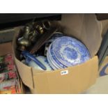 A box containing place mats, blue & white crockery and brass tea and coffee pots