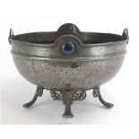 An Arts & Crafts hammered raised bowl decorated with blue roundels, on scrolled feet,