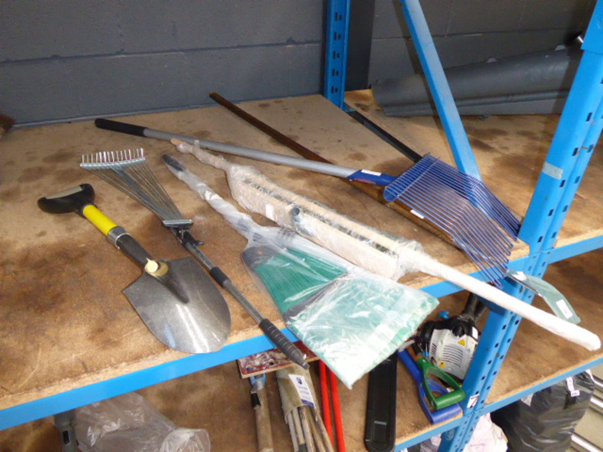 Half a shelf of assorted garden tools including hayforks, hoe, brush, small spade, etc