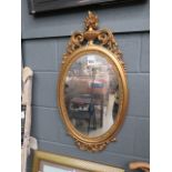 An oval mirror in a decorative gilt frame