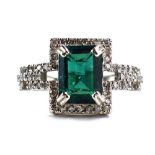 A 14ct white gold ring set emerald cut emerald within a border of small diamonds,