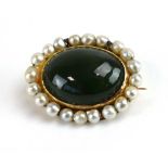 An early 20th century yellow metal brooch of oval form set cabochon green hardstone within a pearl