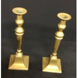 A pair of square based antique brass candlesticks