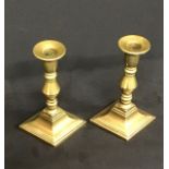 A pair of lozenge based antique brass candlesticks
