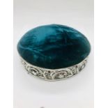 A teal velvet pin or hat pin stand with decorative silver surround