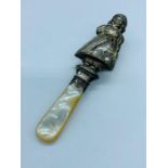 A Mother of Pearl handled and hallmarked silver baby rattle in the form of a little girl (1933)