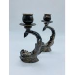 A pair of white metal Maltese candlesticks of dolphin form.