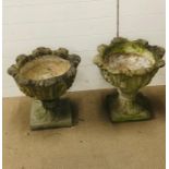A pair of weathered stone garden planters on pedestal base with scroll leaf detailing