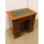 A Kneehole desk with green leather top, a central drawer and six drawers with brass drop handles