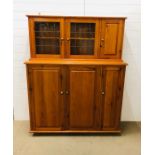 A varnished pine kitchen storage unit with three tall cupboards under and three smaller on top